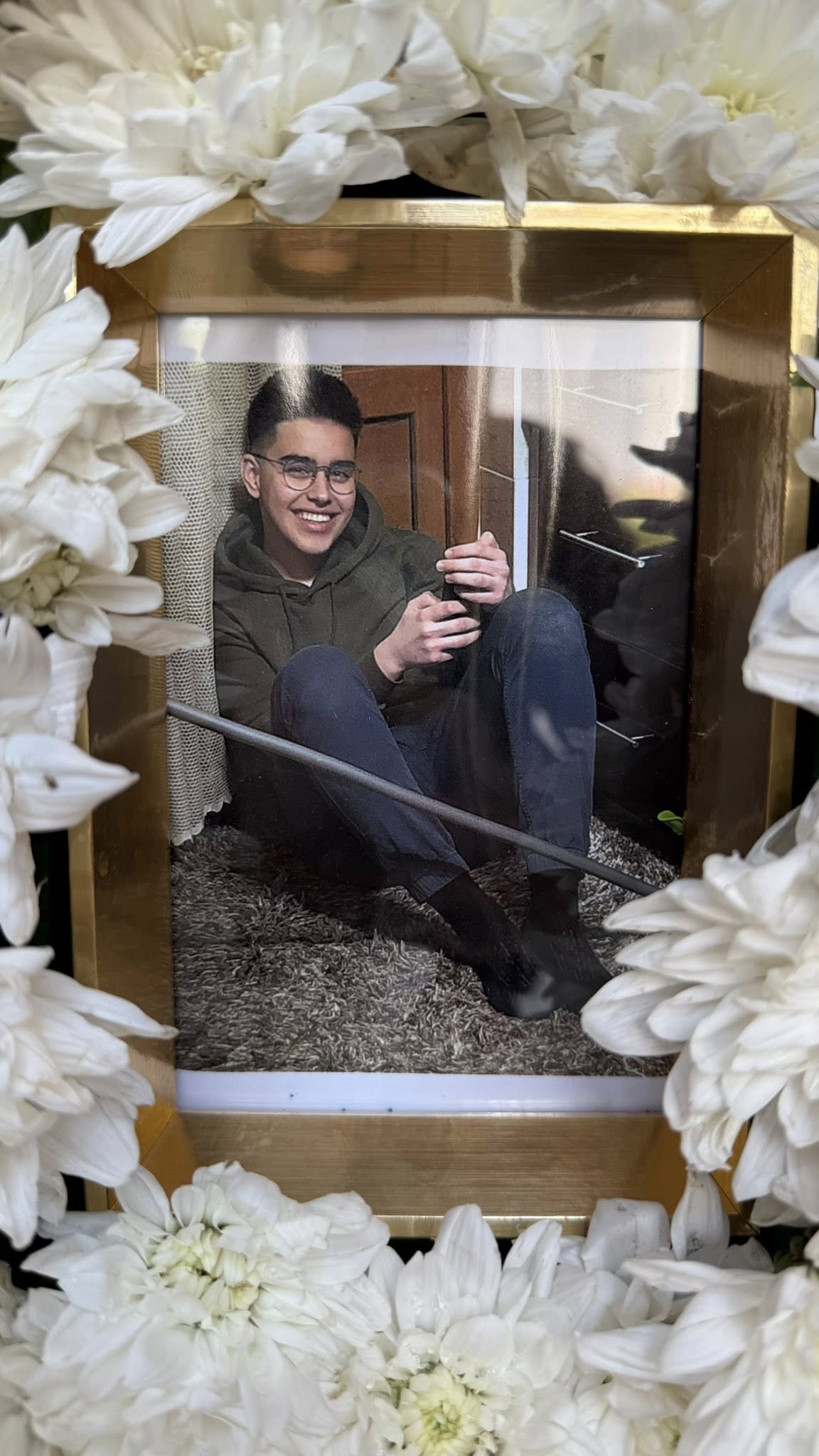 Cruce din flori albe care are în centru o fotografie cu Raul Gabriel Timișag, tânărul de 21 de ani care și-a pierdut viața în Statele Unite