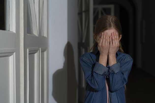 Copilă abuzată, tristă, care își ascunde fața cu palmele