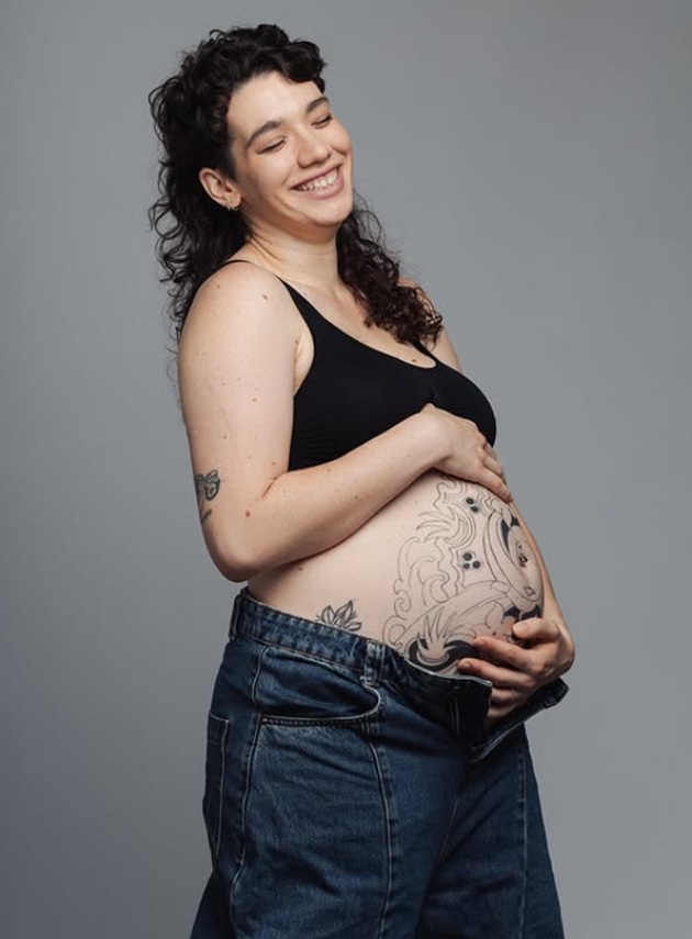 Cabiria Morgenstern, fiica Maiei Morgenstern, zâmbitoare, cuprinzându-și în mâini burta de gravidă, acoperită de tatuaje, cu câteva săptămâni înainte să nască