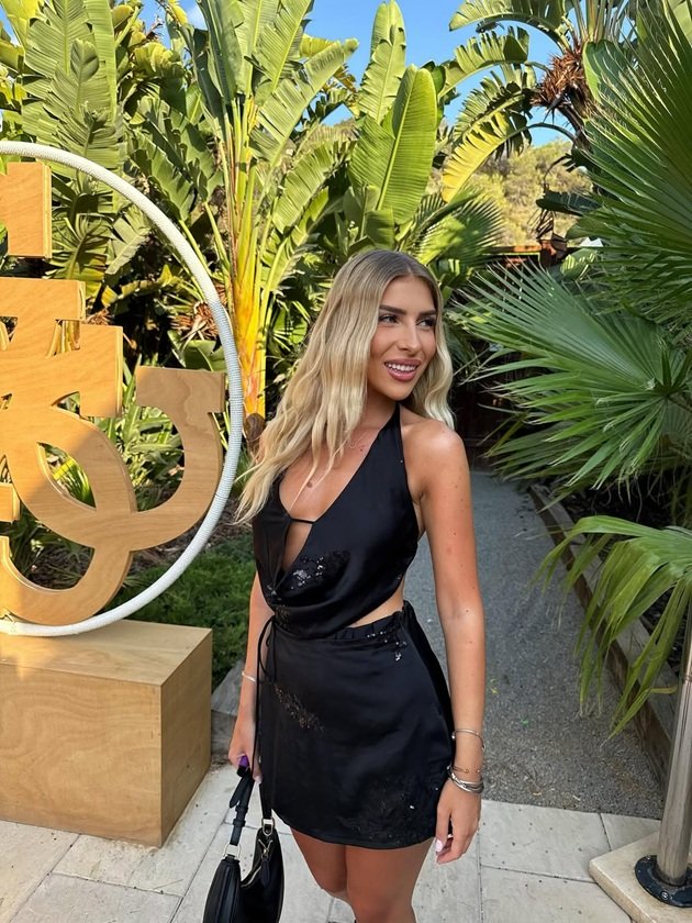 Raluca Jurca, fosta logodnică a lui Cezar Ouatu, într-o rochie mini, neagră, cu paiete, pe o alee plină cu palmieri