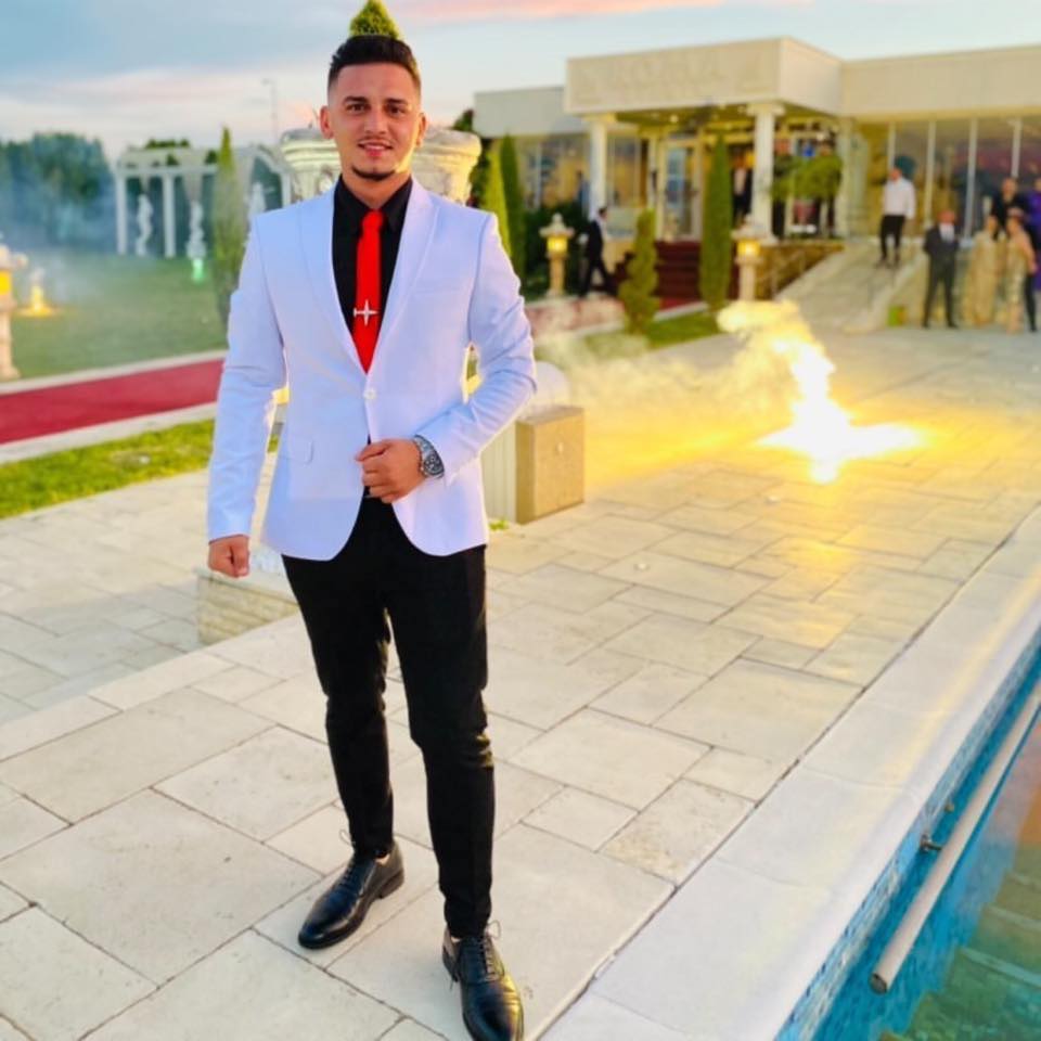 Polițistul Claudiu Savu îmbrăcat în costum, la un eveniment, ținându-se cu mâna de o parte a sacoului deschis la culoare, combinat cu pantaloni negri