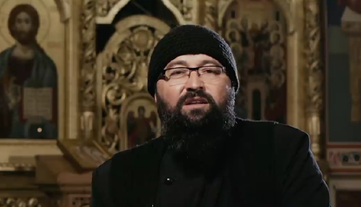 Preotul Visarion Alexa în biserică, în straie preoțești, cu o căciulă neagră pe cap