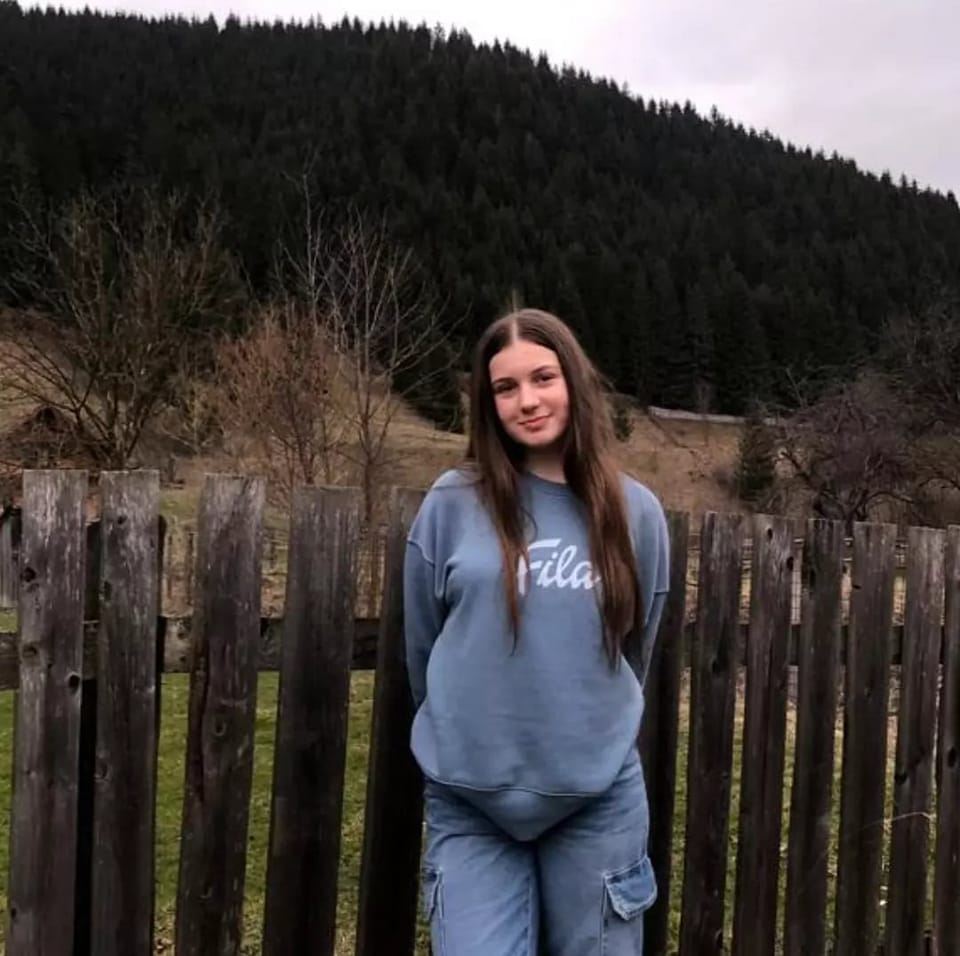 Cornelia Semeniuc cu mâinile la spate, îmbrăcată în albastru, cu părul lung și desfăcut, sprijinindu-se de un gard de lemn