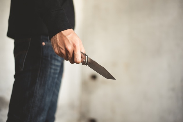 Bărbat în blugi și cămașă neagră care ține în mână un cuțit