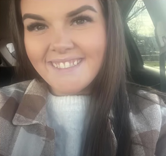 Profesoara Elena Bardin făcându-și un selfie în mașină, zâmbitoare, purtând un pulover alb și o jachetă în carouri