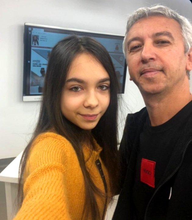 Dan Diaconescu zâmbitor, îmbrăcat în negru, în biroul unei televiziuni, alături de fiica sa, Dona Diaconescu, cu părul desfăcut, îmbrăcată într-un pulover galben