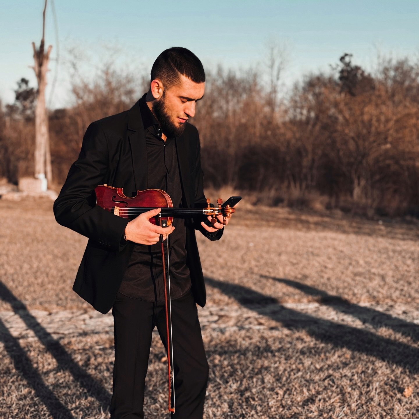 Cristian Botgros, nepotul lui Nicolae Botgros, la marginea unei păduri, cu o vioară în mână și telefonul în cealaltă mână, îmbrăcat într-un costum negru și cămașă neagră