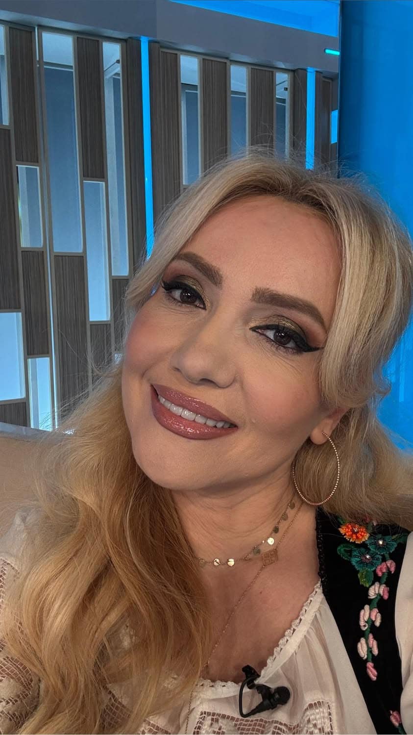 Adriana Ochișanu zâmbitoare, făcându-și un selfie în costum popular, cu bijuterii aurii la gât și în urechi
