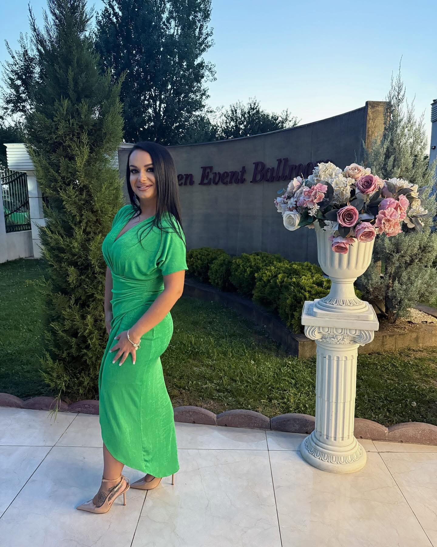 Andreea Tone, în rochie verde elegantă și pantofi nude, la un eveniment, făcându-și o fotografie în curtea unui restaurant decorat pentru o petrecere