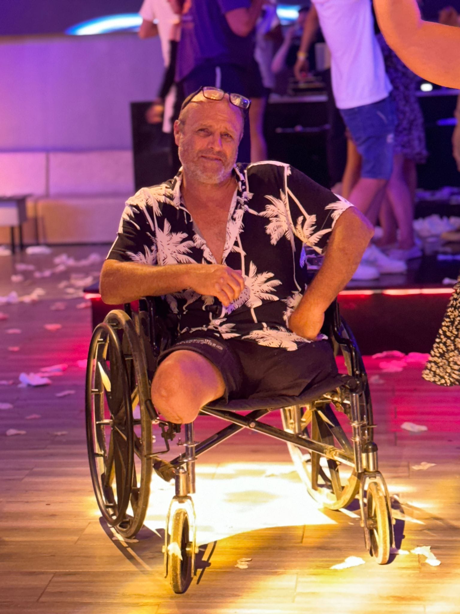 Mihai Palaghiea în scaun cu rotile, îmbrăcat în pantaloni scurți negri și cămașă neagră cu frunze albe, imagine în care se vede că are ambele picioare amputate