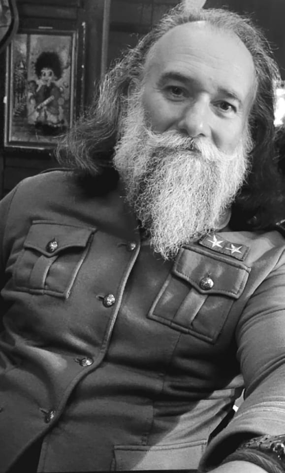 Imagine alb-negru cu Marius Keseri, regretatul baterist al trupei Direcția 5, îmbrăcat într-o haină militară, cu barbă lungă și păr lung 