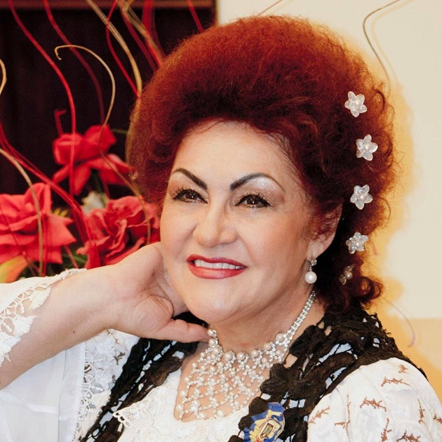 Elena Merișoreanu zâmbitoare, în costum popular, cu agrafe în formă de floare în păr, ținându-și mâna sub bărbie