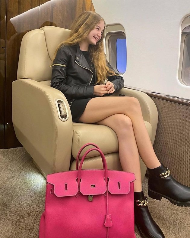 Irina Columbeanu în avion, zâmbitoare, îmbrăcată într-o rochie neagră mini și cu geacă de piele pe deasupra
