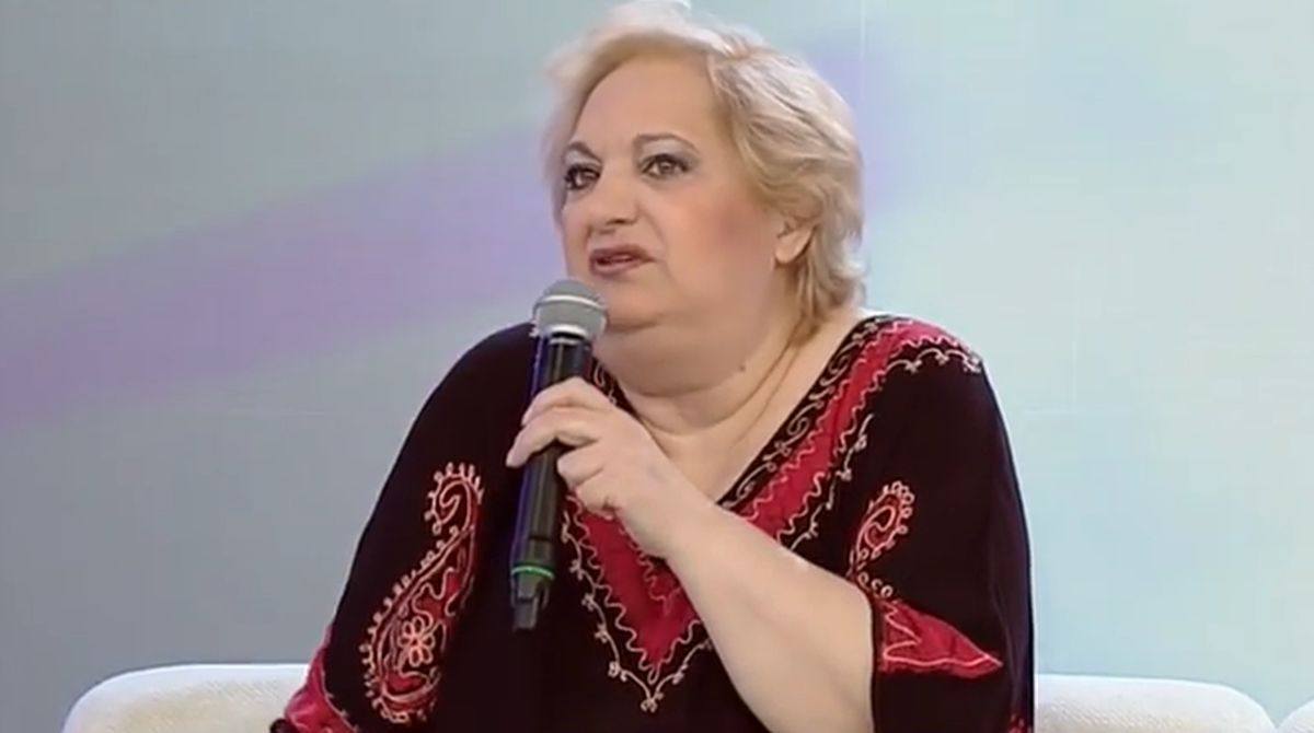 Marinela Chelaru vorbind la microfon, într-un platou de televiziune, în timpul unei emisiuni, îmbrăcată într-o rochie neagră cu roșu