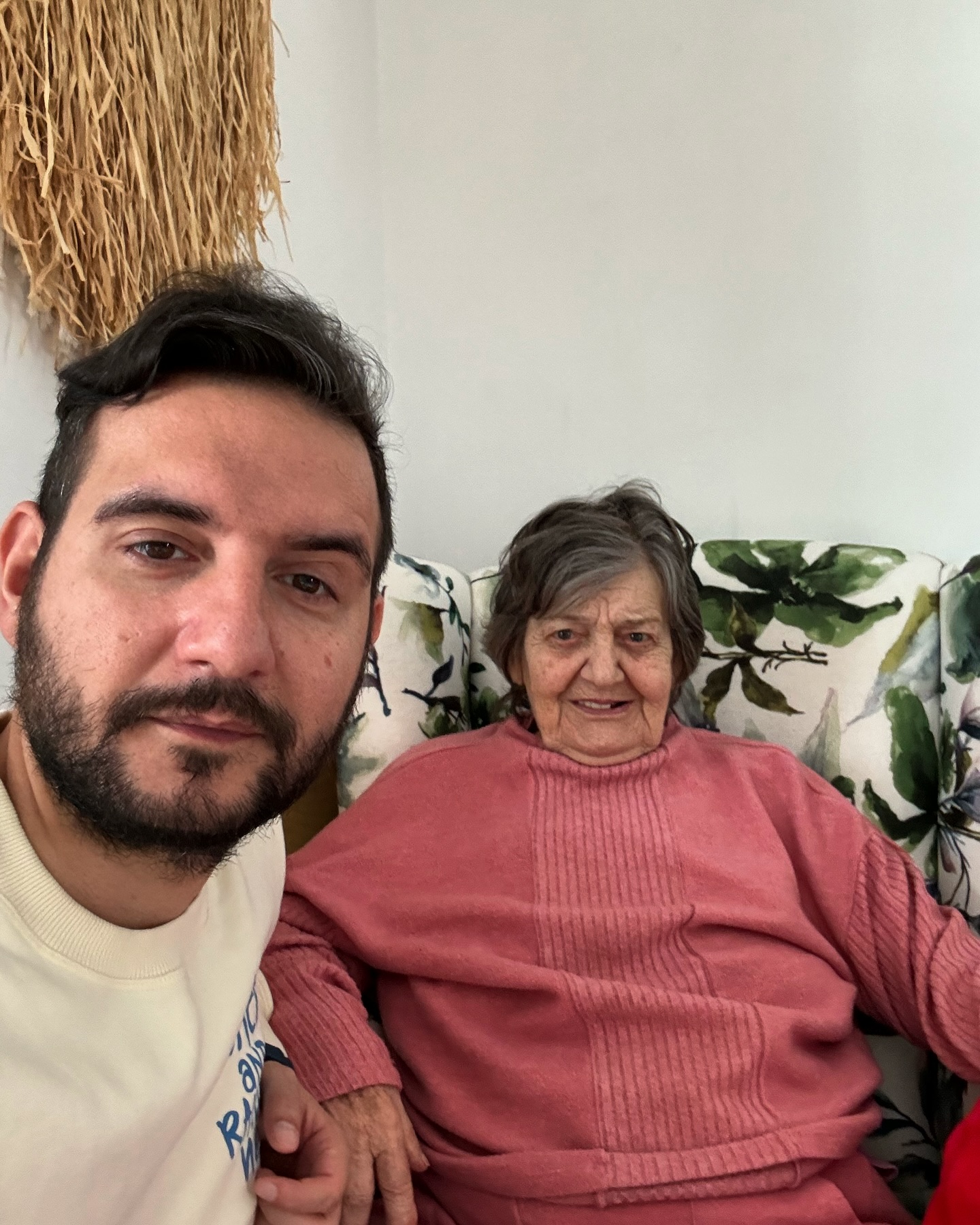 Adrian Cuculis în tricou alb, stând pe canapea lângă bunica lui zâmbitoare, îmbrăcată în roz