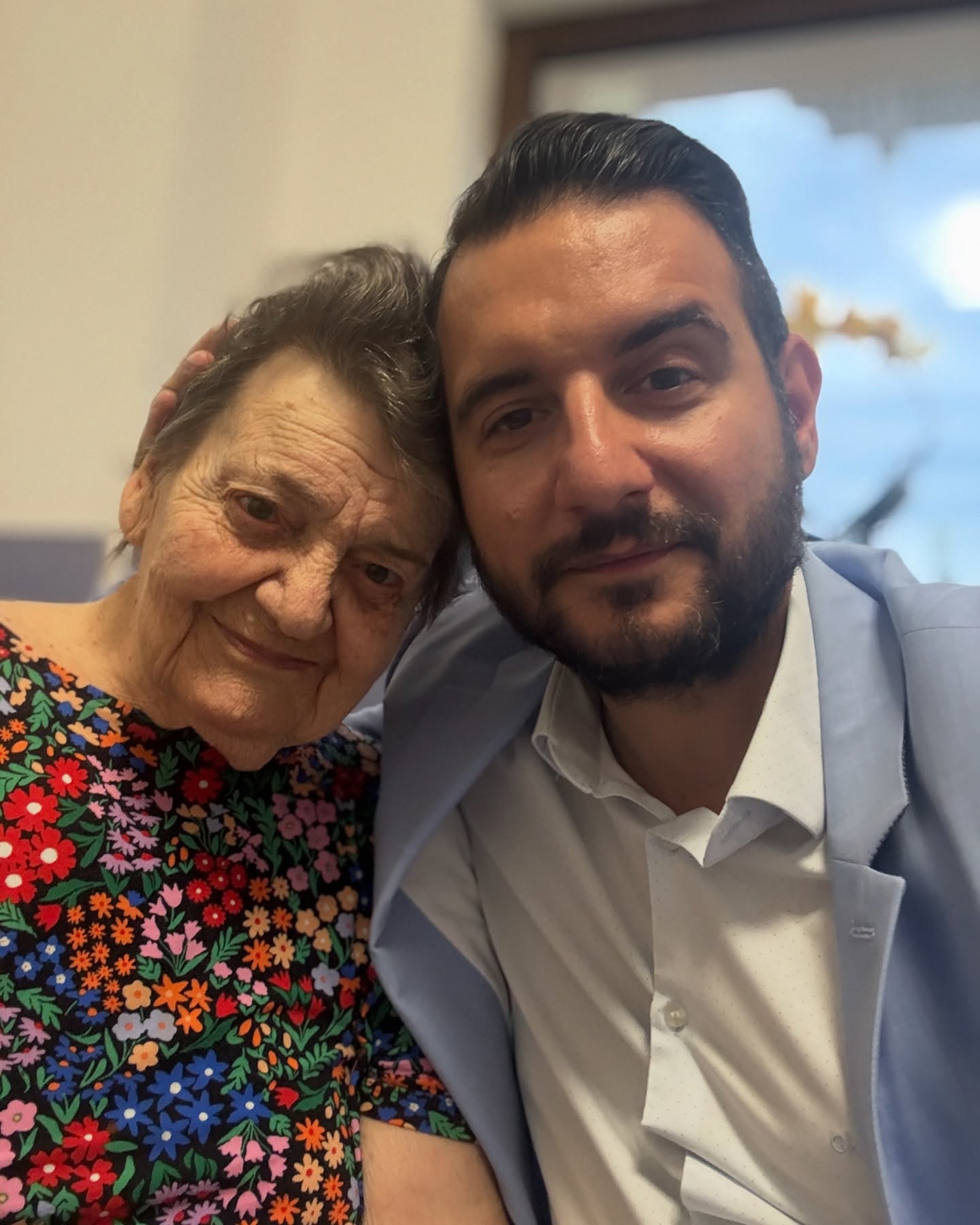 Adrian Cuculis în costum bleu și cămașă albă, făcându-și un selfie alături de bunica lui, îmbrăcată într-un tricou negru cu flori colorate