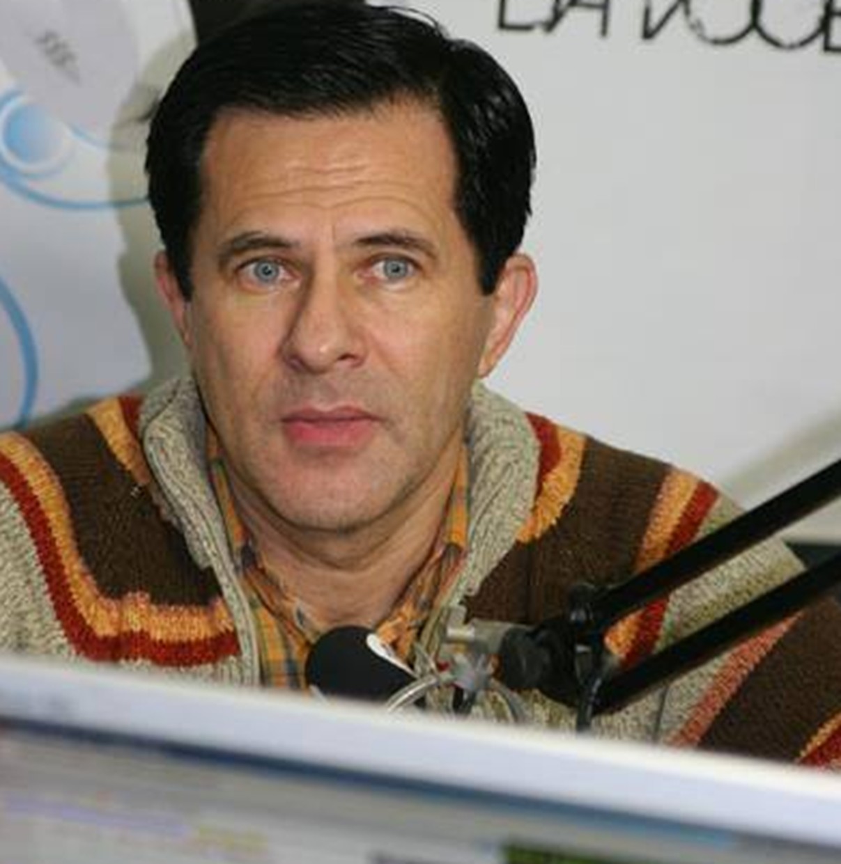 Doru Octavian Dumitru într-un studio de radio, vorbind la microfon, îmbrăcat într-un pulover colorat în nuanțe de bej, maro, portocaliu și vișiniu