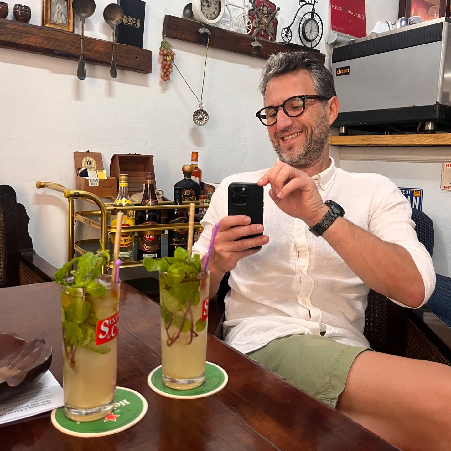 Andi Moisescu relaxat și zâmbitor, lângă două cocktailuri, cărora le făcea o fotografie cu telefonul