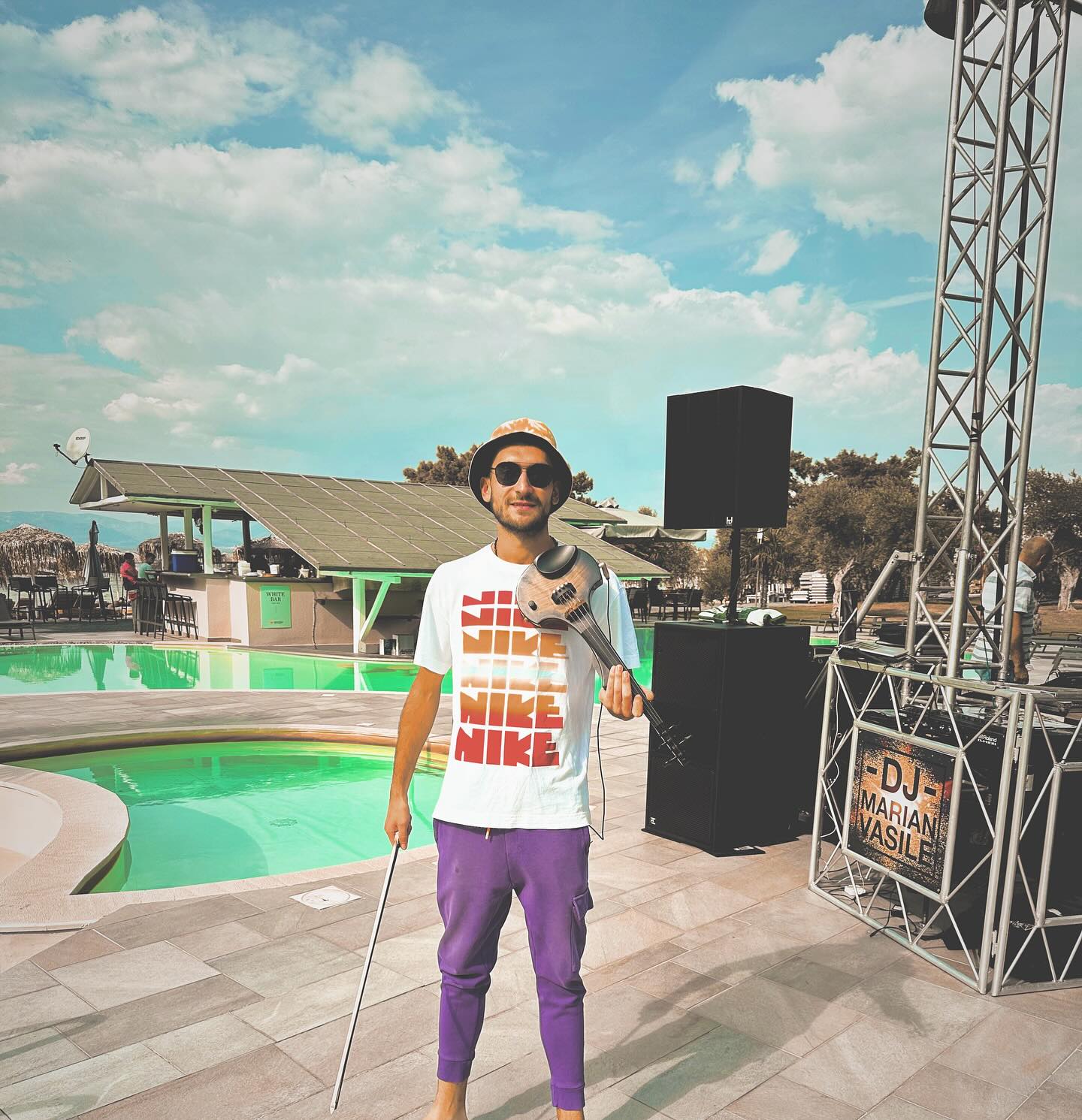 Cristian Botgros cu vioara și arcușul în mână pe marginea unei piscine, unde este amplasată o scenă pe care urma să cânte