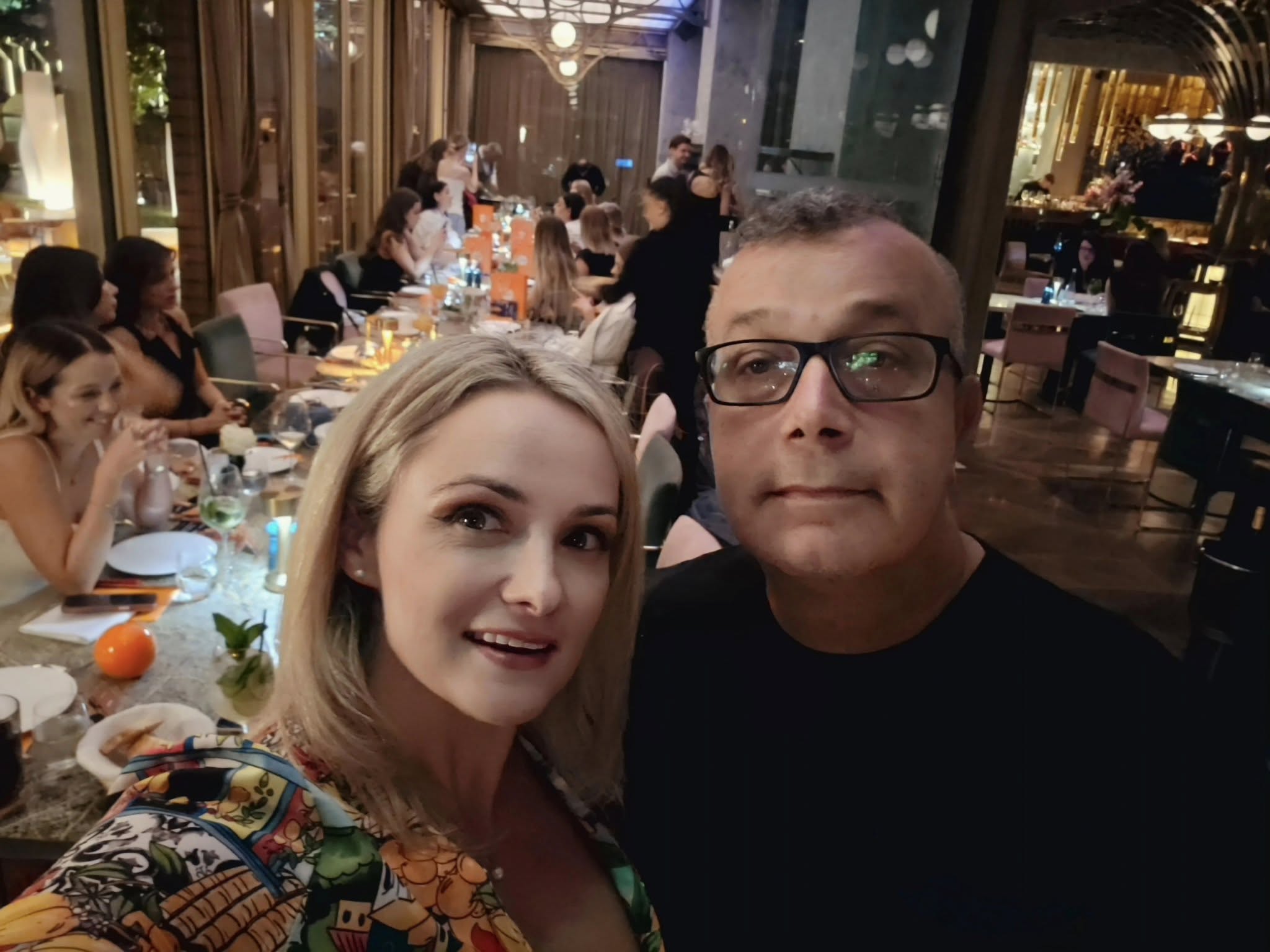 Amalia și Domenico Bellantoni lângă o masă, în restaurant, fotografiindu-se alături de ceilalți oameni prezenți
