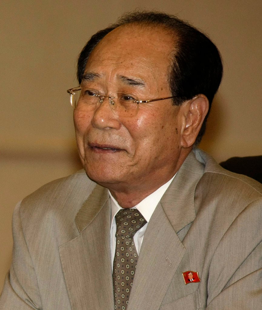 Kim Yong Nam, fostul șef de stat ceremonial din Coreea de Nord, îmbrăcat în costum gri și cămașă albă, purtând la gât o cămașă cu imprimeu floral și ochelari de vedere la ochi