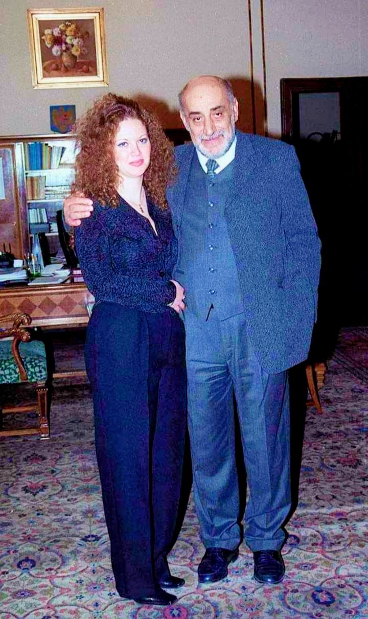 Oana și Viorel Lis când erau mai tineri, îmbrăcați în gri, stând în fața unei biblioteci