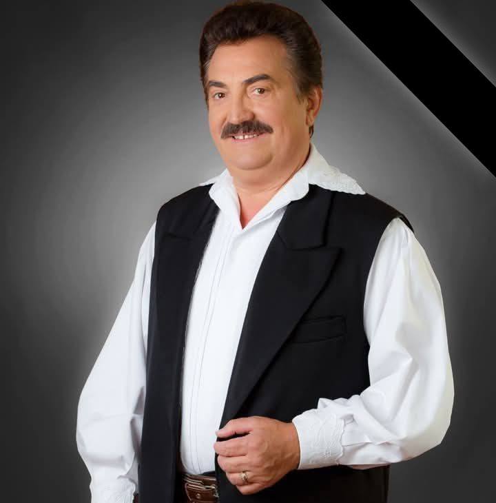 Petrică Mîțu Stoian zâmbitor, îmbrăcat în ținuta de scenă care l-a consacrat, cu ie albă și vestă neagră