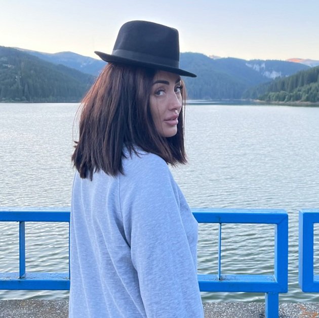 Nidia Moculescu, fiica lui Horia Moculescu, pe malul unui lac, între munți, purtând o pălărie neagră pe cap