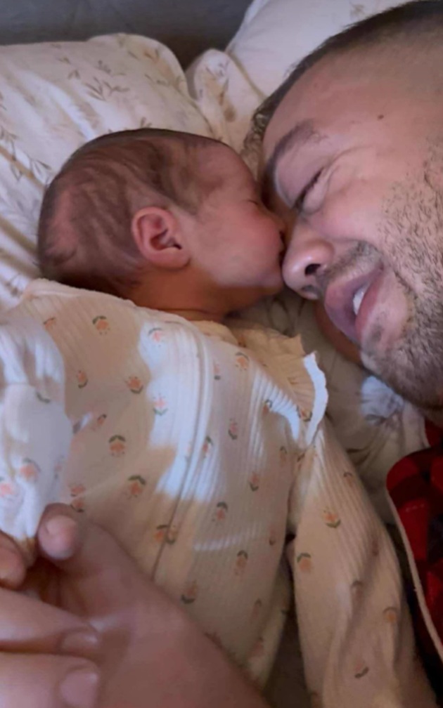 Nelu Mic fericit, stând în pat, cu capul pe pernă, alături de fetița sa nou-născută