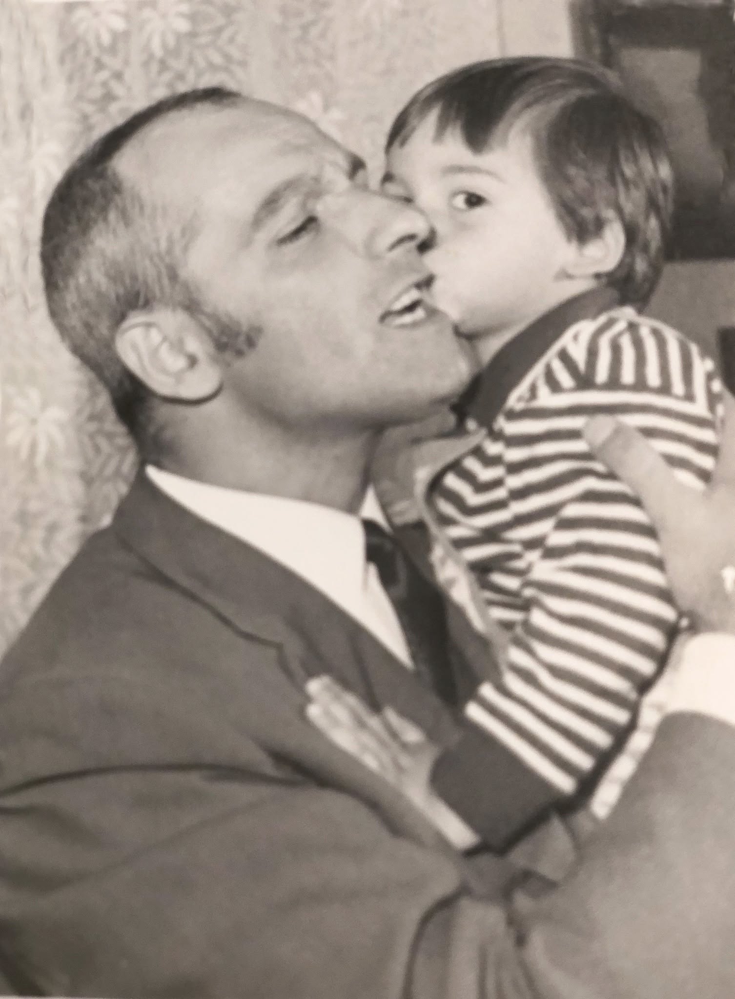 Imagine alb-negru cu Ștefan Bănică Senior care îl ține în brațe pe Ștefan Bănică Junior, în timp ce acesta îl sărută pe obraz