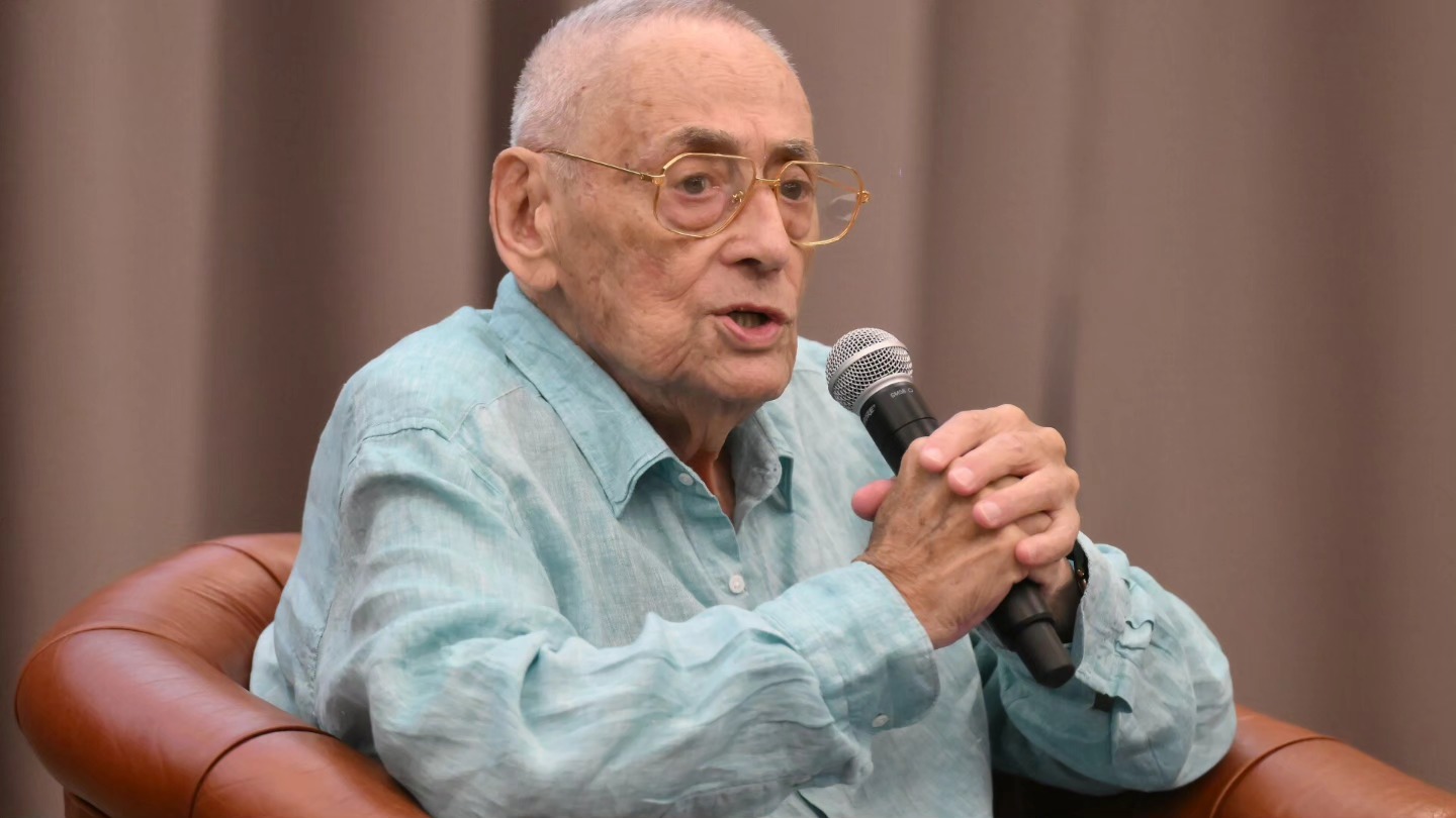 Horia Moculescu la bătrânețe, vizibil slăbit, stând pe un fotoliu și vorbind la microfon în fața publicului său, îmbrăcat într-o cămașă bleu