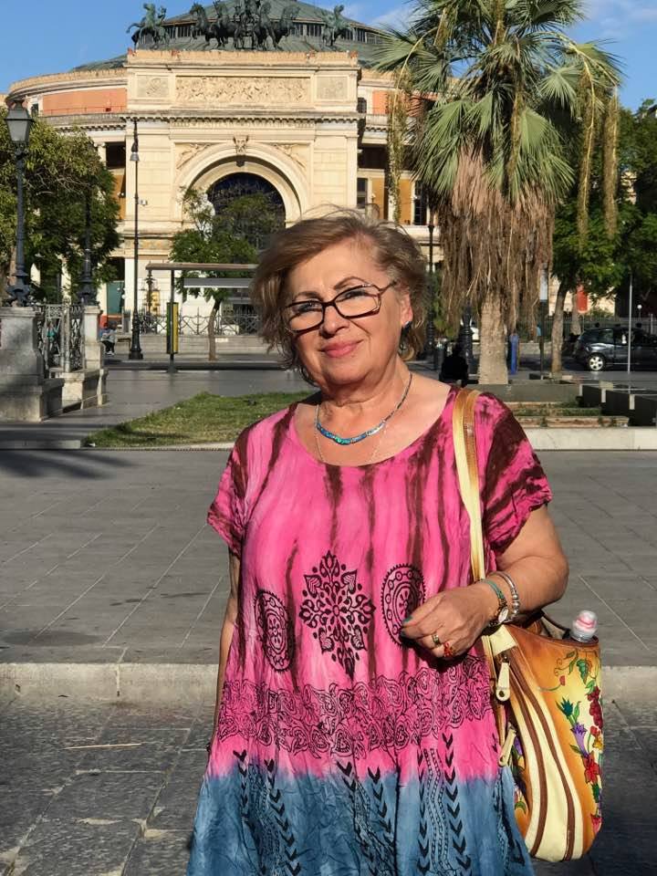 Angela Zahiu în timpul unei vacanțe, îmbrăcată într-o rochie în nuanțe de roz și albastru, purtând o geantă colorată pe umăr