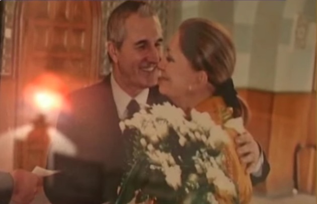 Gheorghe Dinică în costum, cu cravată, cuprinzând-o în brațe pe soția sa, Gabriela Dinică, care ține în mâini un buchet mare de flori albe