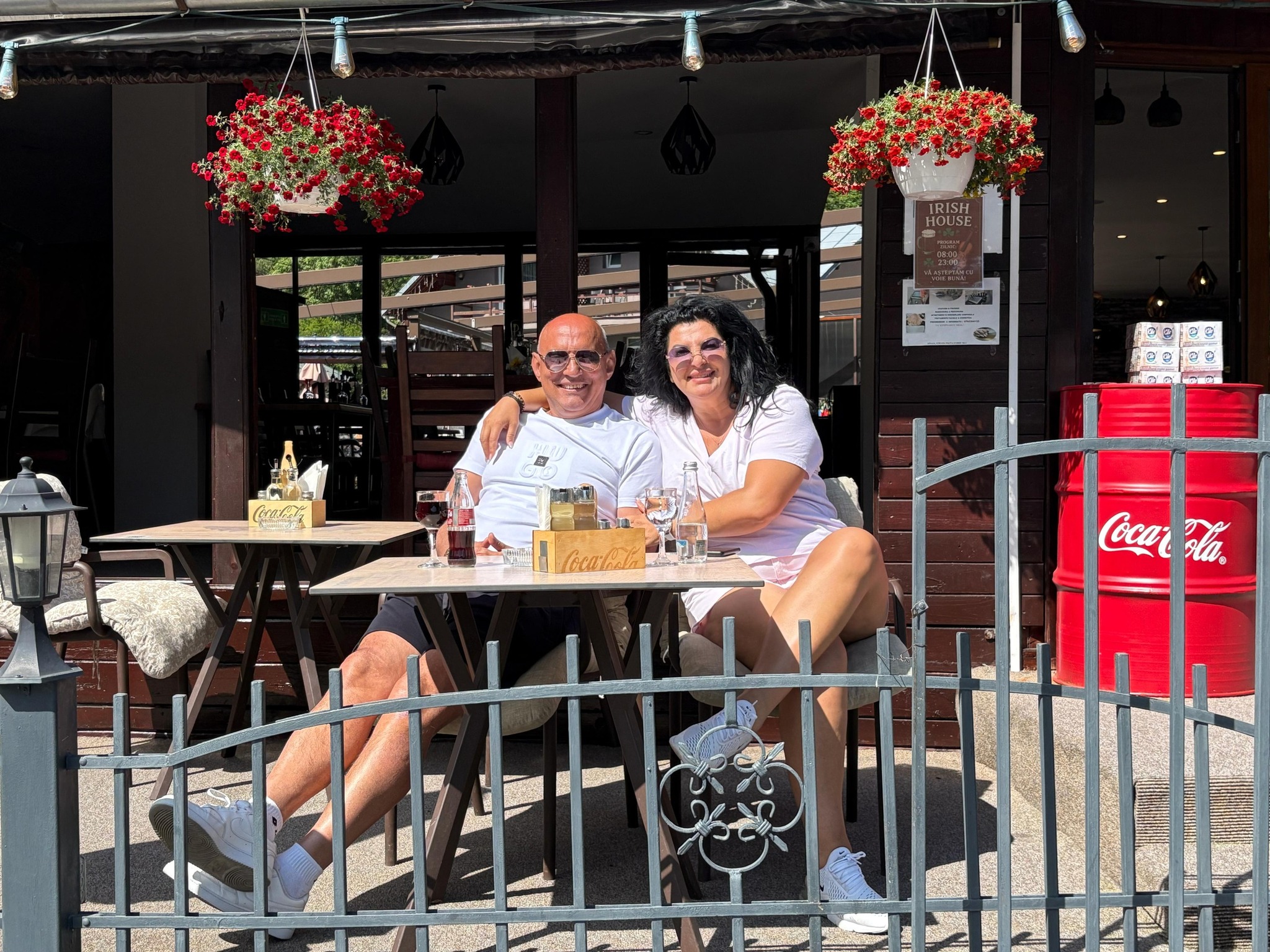 Florin Prunea și Lăcrămioara Ursu îmbrățișați, stând la soare, la masa de pe terasa unui restaurant