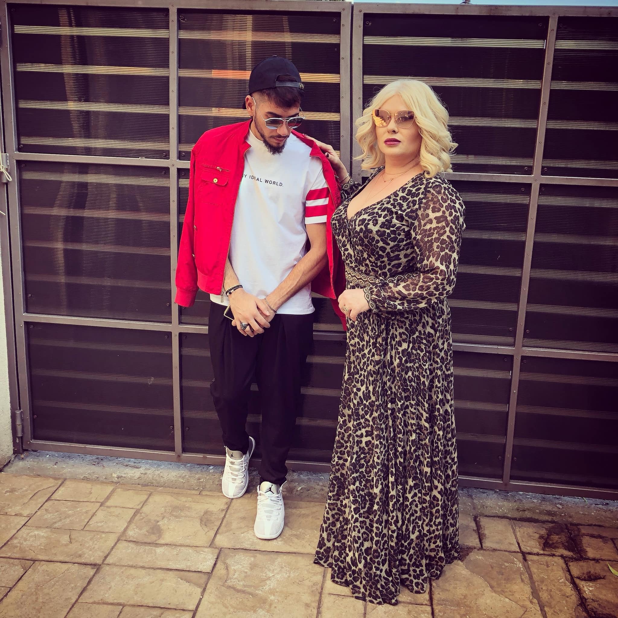 Fulgy de la Clejani, îmbrăcat în negru, alb și roșu, cu ochelarii de soare la ochi, alături de mama sa, Viorica de la Clejani, îmbrăcată într-o rochie lungă cu animal print, purtând ochelari de soare maro