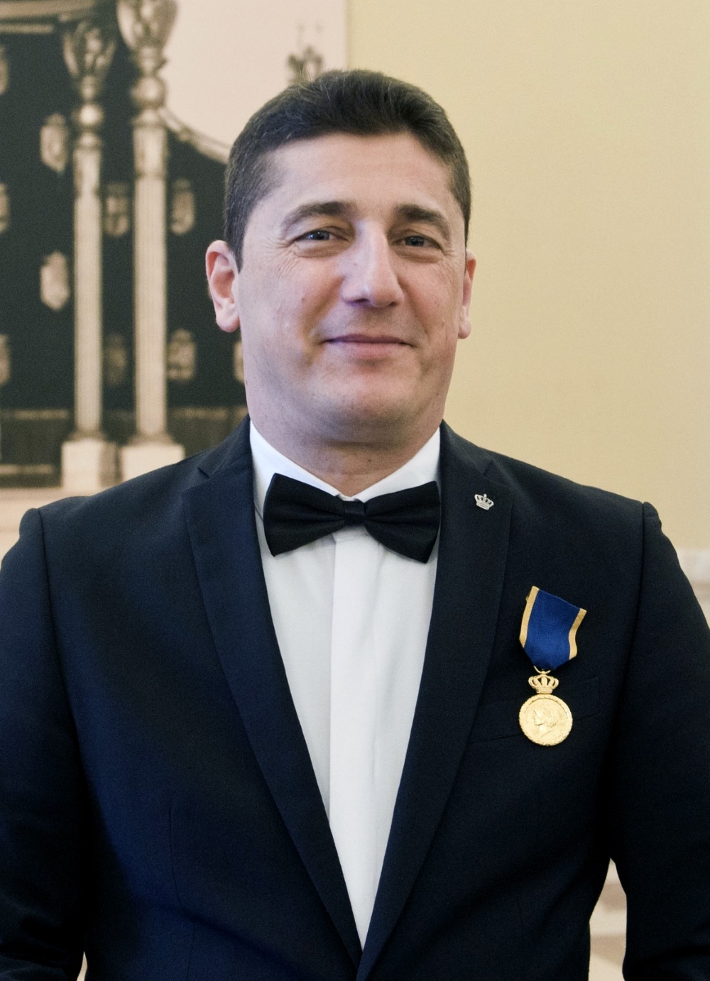 Mihai Bașturea în costum închis la culoare, cu papion negru la gât, purtând în piept Medalia Regală pentru loialitate