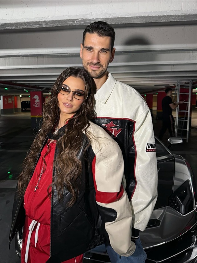 Theo Rose și soțul ei, Anghel Damian, stând îmbrățișați într-o parcare, îmbrăcați asortat, în negru, alb și roșu, cu geci de piele similare