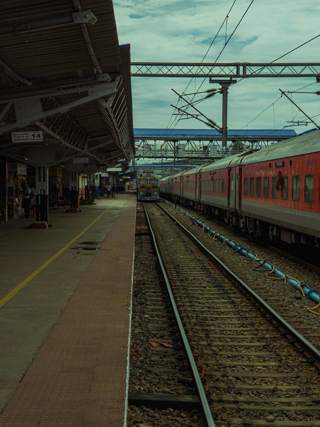 Tren care sosește în gară, în timp ce unii călători așteaptă pe peron