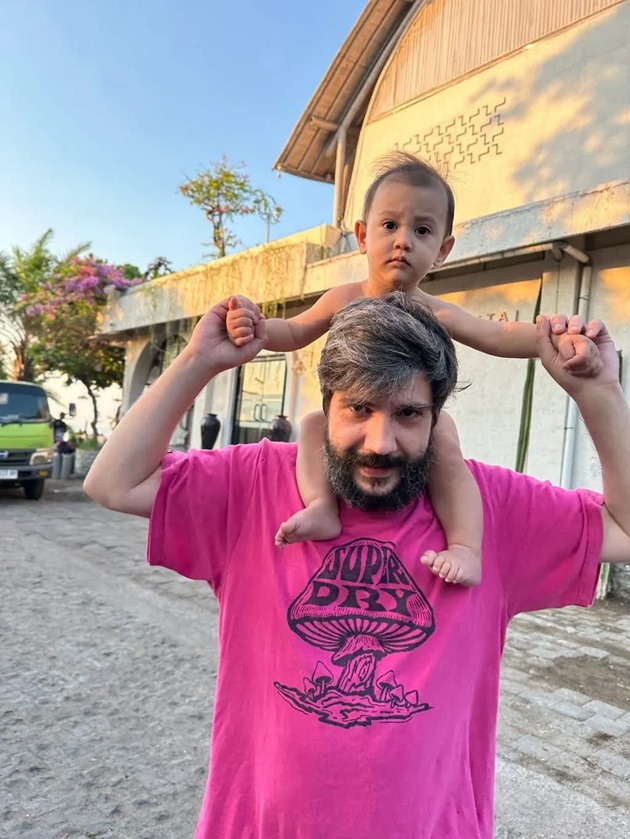 Rareș Tomache într-un tricou roz, ținându-l pe umeri pe băiețelul său de un an