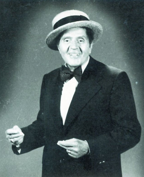 Imagine alb-negru cu Gică Petrescu vesel, &icirc;n lumina reflectoarelor, țin&acirc;ndu-și degetele apropiate, &icirc;n timp ce era &icirc;mbrăcat &icirc;ntr-un costum &icirc;nchis la culoare și avea pe cap o pălărie deschisă la culoare, cu bandă neagră.