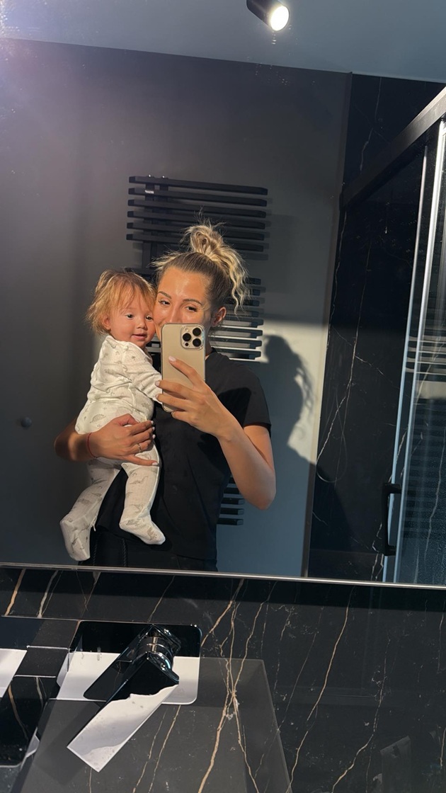 Claudia Puican în baie, îmbrăcată în negru, făcându-și o fotografie în oglindă, în timp ce îl ținea în brațe pe fiul ei îmbrăcat în alb