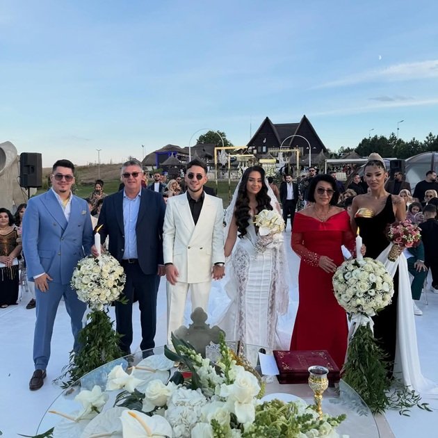 Tony One (Biju) și soția sa Antonia în ziua nunții, îmbrăcați amândoi în alb, în mire și mireasă, alături de nașii lor, părinții lui Bogdan de la Ploiești și Bogdan de la Ploiești alături de Cristina Pucean