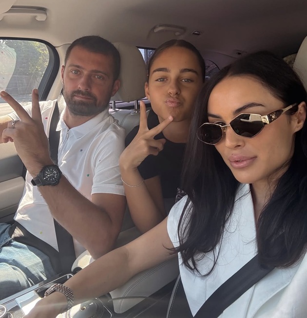 Gabi Tamaș în mașină, cu o mână pe volan, în timp ce lângă el stă soția sa Ioana, iar în spatele lor se află fiica lor Selena