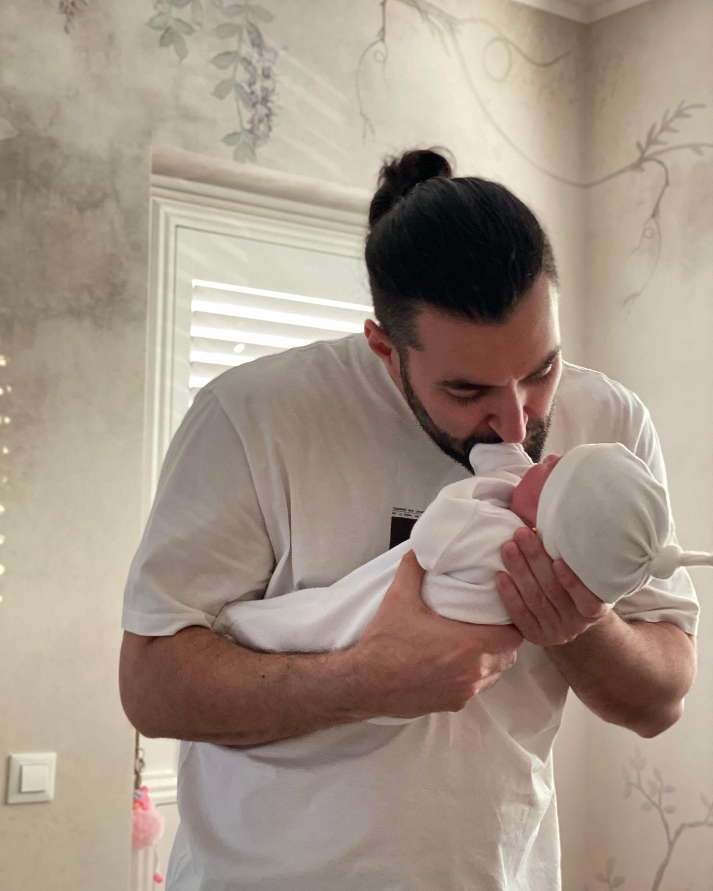 Smiley ținându-și în brațe fiica nou-născută, în camera acesteia, cu tapet personalizat pentru fetițe