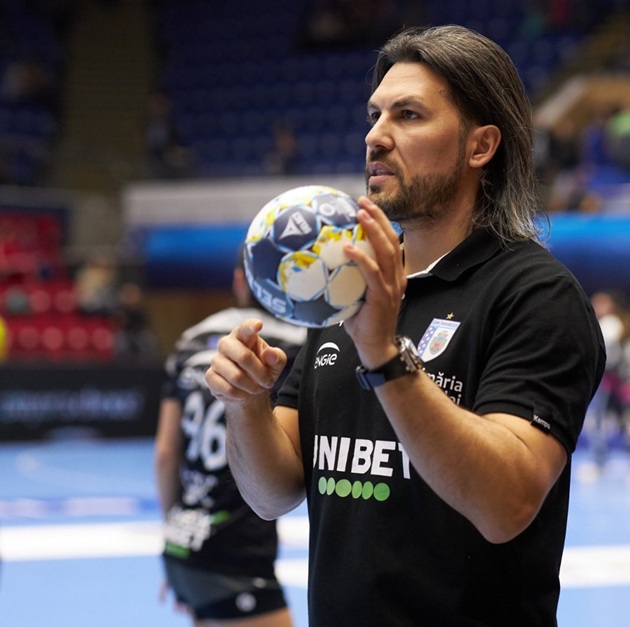 Adi Vasile în teren, cu mingea de handbal în mână, arătând echipei pe care o antrena ce are de făcut