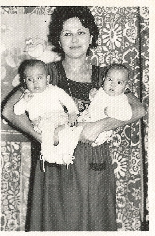 Imagine alb-negru cu gemenele Modorcea în copilărie, alături de mama lor, Violeta Modorcea, care le ținea în brațe, lângă o draperie cu flori