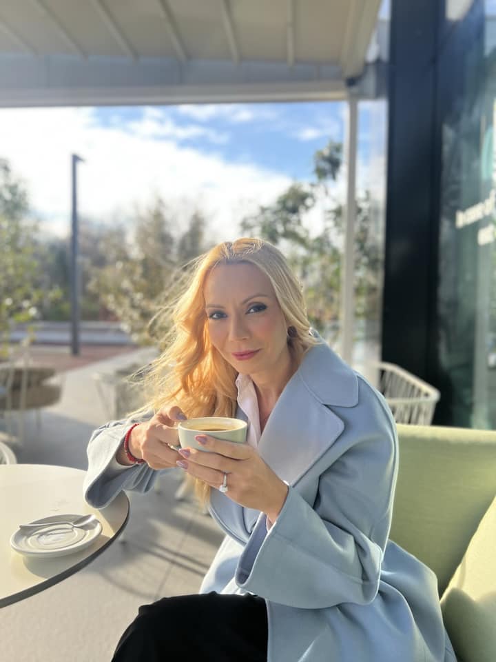 Daciana Sârbu într-un palton lung, bleu, pe terasa unei cafenele, savurând o cafea