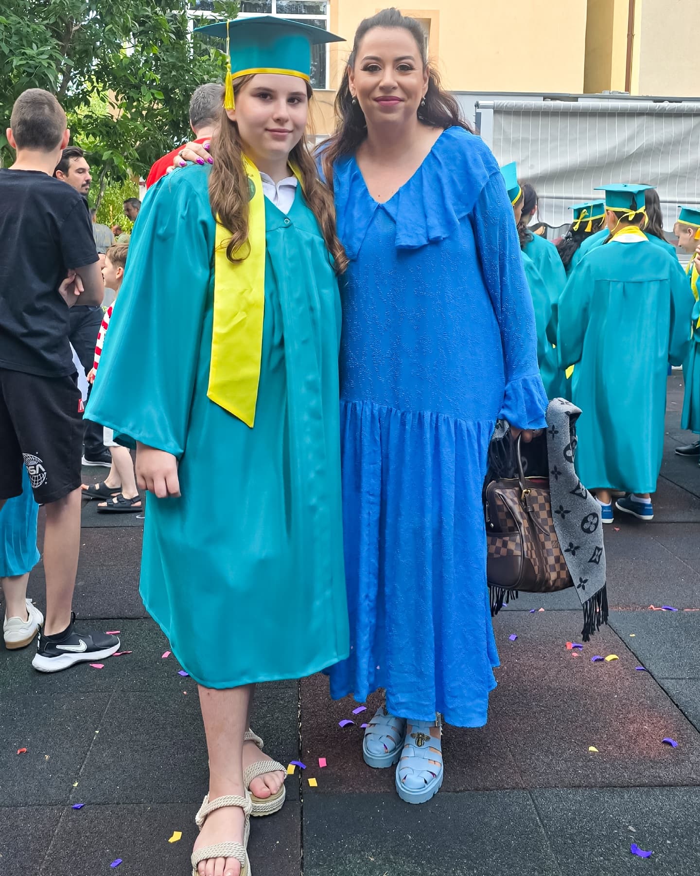 Oana Roman ținând-o de gât pe fiica ei, Isabela, în ziua absolvirii, în timp ce aceasta din urmă este îmbrăcată în robă și poartă tocă pe cap.