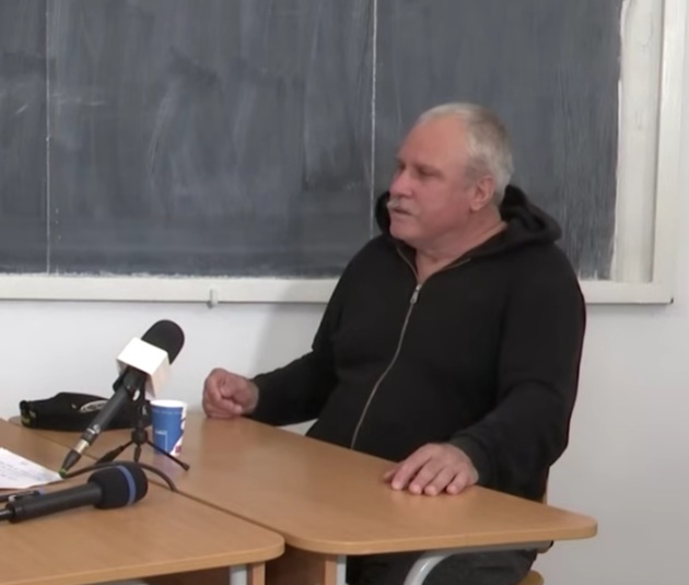 Gheorghe Dincă în penitenciar, stând de vorbă cu un reporter, având microfonul în față, în sala în care deținuții primesc vizite