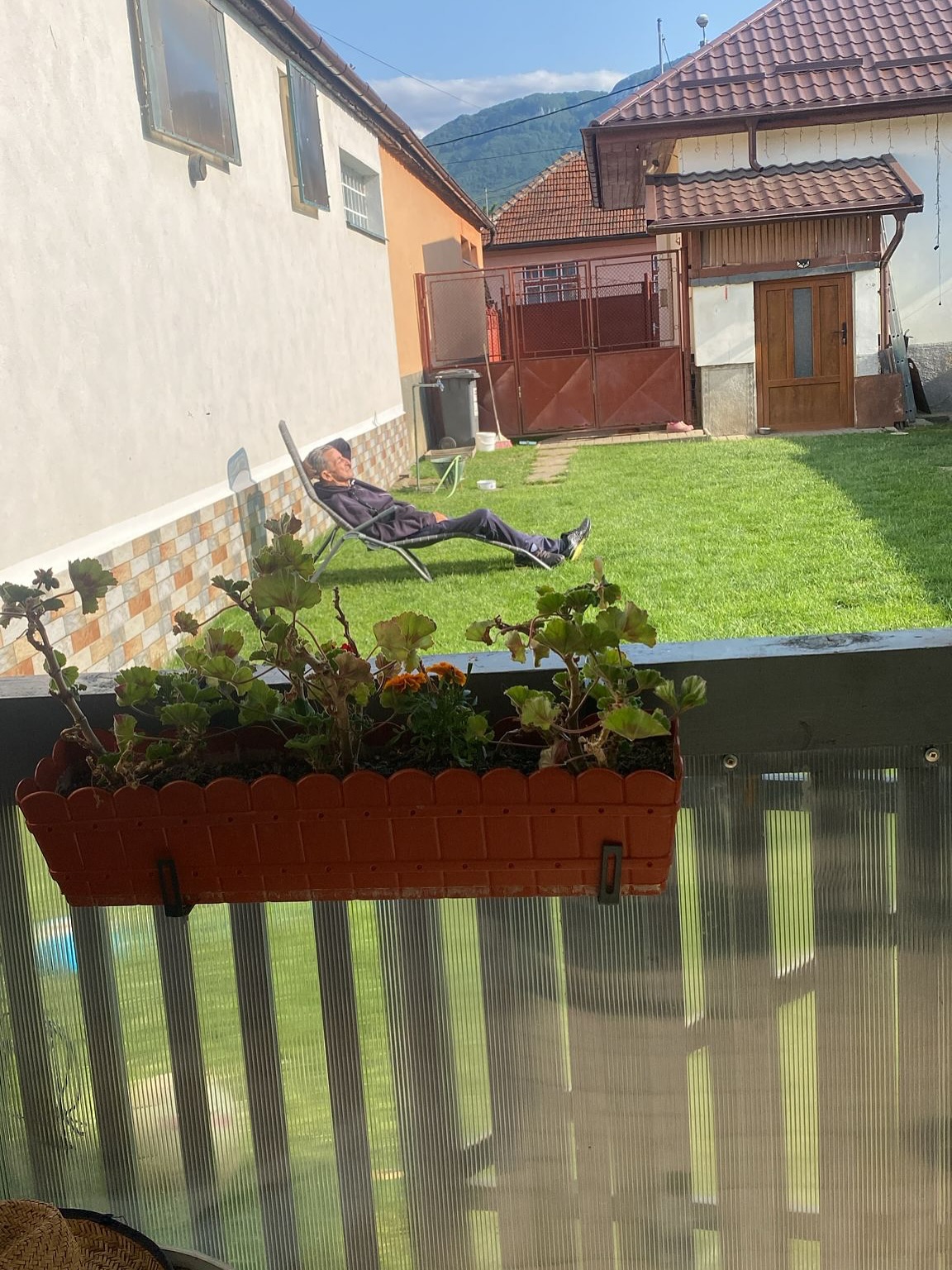 Tatăl Ioanei Blaj stând în curte, la soare, pe un șezlong, cu una dintre mâini sub cap, îmbrăcat într-un trening gri închis